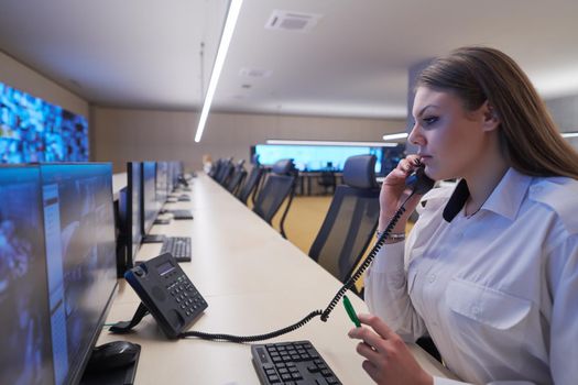 Female security guard operator talking on the phone while working at workstation with multiple displays Security guards working on multiple monitors