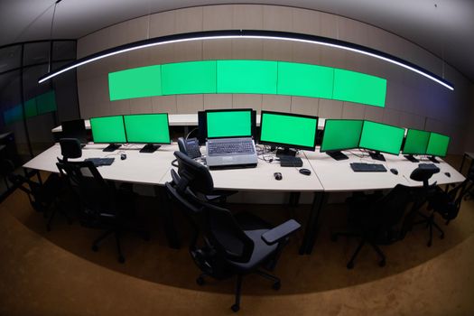 Empty interior of big modern security system control room with blank green screens, workstation with multiple displays, monitoring room with at security data center  Empty office, desk, and chairs at a main CCTV security data center