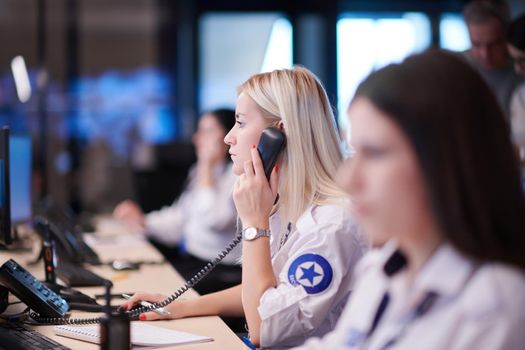 Female security guard operator talking on the phone while working at workstation with multiple displays Security guards working on multiple monitors