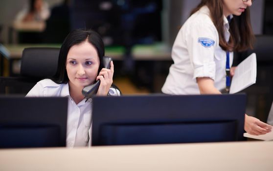 Female security guard operator talking on the phone while working at workstation with multiple displays Security guards working on multiple monitors