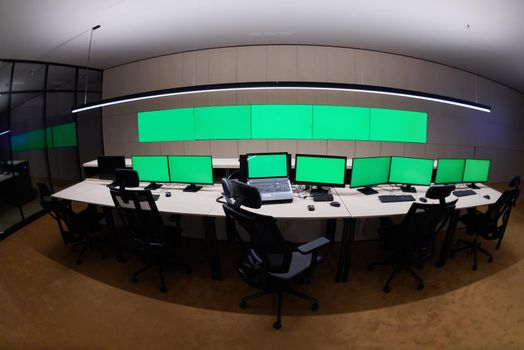 Empty interior of big modern security system control room with blank green screens, workstation with multiple displays, monitoring room with at security data center  Empty office, desk, and chairs at a main CCTV security data center