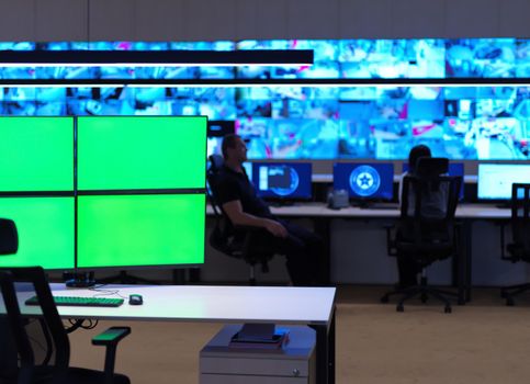 interior of big modern security system control room with blank green screens, workstation with multiple displays, monitoring room with at security data center  Empty office, desk, and chairs at a main CCTV security data center