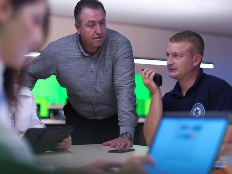 Group of security guards sitting and having briefing In the system control room  They're working in security data center surrounded by multiple Screens