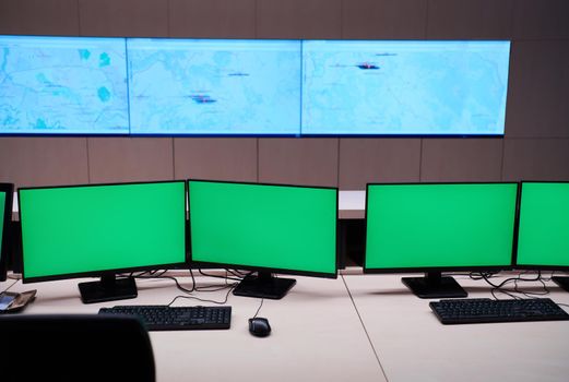Empty interior of big modern security system control room with blank green screens, workstation with multiple displays, monitoring room with at security data center  Empty office, desk, and chairs at a main CCTV security data center