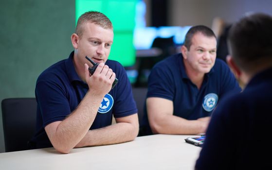 Group of security guards sitting and having briefing In the system control room  They're working in security data center surrounded by multiple Screens