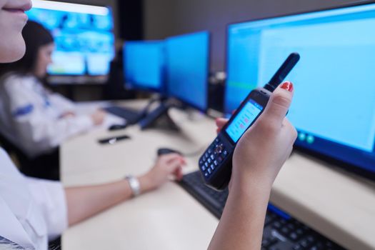 Female security operator holding portable radio in hand while working in a data system control room offices Technical Operator Working at  workstation with multiple displays, security guard working on multiple monitors