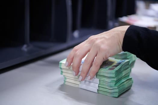 Bank employees using money counting machine while sorting and counting paper banknotes inside bank vault. Large amounts of money in the bank