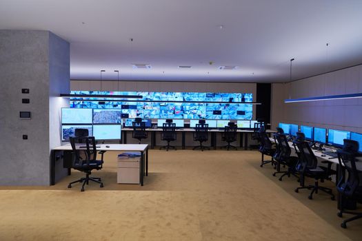 Empty interior of big modern security system control room, workstation with multiple displays, monitoring room with at security data center  Empty office, desk, and chairs at a main CCTV security data center