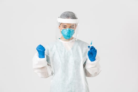 Covid-19, coronavirus disease, healthcare workers concept. Determined and confident female asian doctor, tech lab employee in personal protective equipment holding syringe with vaccine.