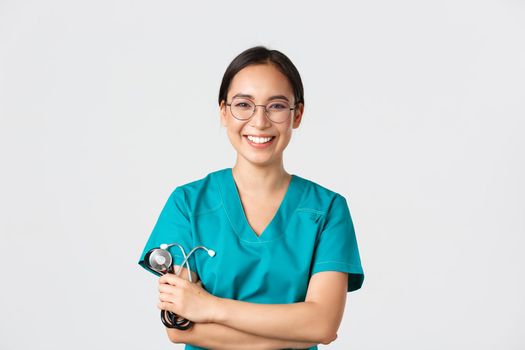 Covid-19, coronavirus disease, healthcare workers concept. Confident happy asian female physician, doctor in glasses, cross arms chest and smiling, holding stethoscope for examination.
