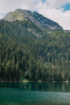 Beautiful view of emerald lake. Clear turquoise water reflect the snow-capped mountain, tall pine trees that line the shore and white clouds in a blue sky