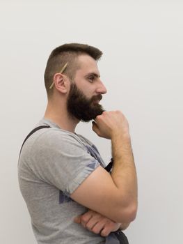portrait of bearded hipster handyman with pen behind ear isolated on white background