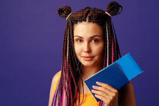 Young woman hippie holding passport and map in her hands against purple background. Travelling and lifestyle concept