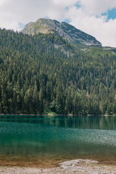 Beautiful view of emerald lake. Clear turquoise water reflect the snow-capped mountain, tall pine trees that line the shore and white clouds in a blue sky