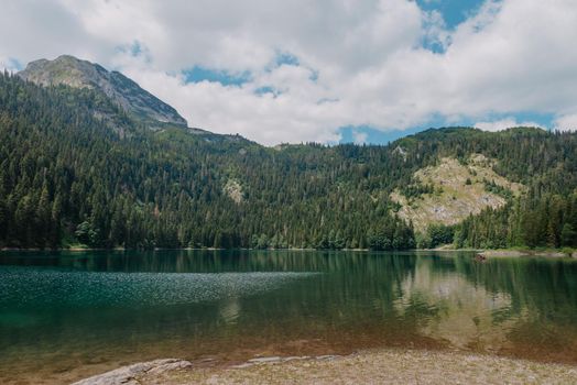 Beautiful view of emerald lake. Clear turquoise water reflect the snow-capped mountain, tall pine trees that line the shore and white clouds in a blue sky