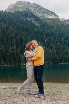 Romantic wedding couple in love standing on the stony shore of the lake, Scenic mountain view. The bride and groom. Beautiful caucasian couple hugging by the lake at summer sunny day. Honeymoon concept.