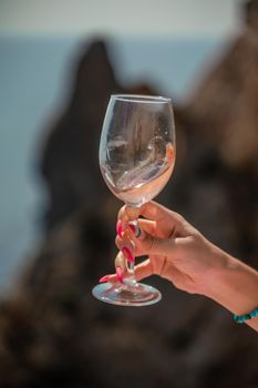 A female hand holds a glass of wine against the background of the sea and mountains