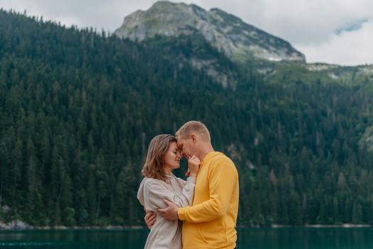 Romantic wedding couple in love standing on the stony shore of the lake, Scenic mountain view. The bride and groom. Beautiful caucasian couple hugging by the lake at summer sunny day. Honeymoon concept.