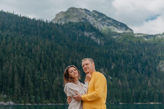 Romantic wedding couple in love standing on the stony shore of the lake, Scenic mountain view. The bride and groom. Beautiful caucasian couple hugging by the lake at summer sunny day. Honeymoon concept.