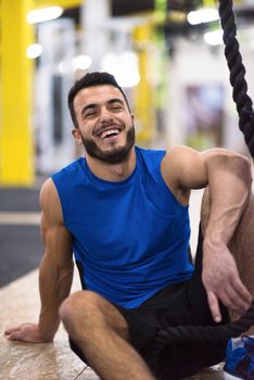 young muscular man sitting and relaxing before rope climbing in cross fitness gym