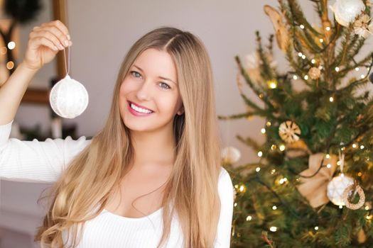 Decorating Christmas tree and winter holidays concept. Happy smiling woman holding festive ornament at home.