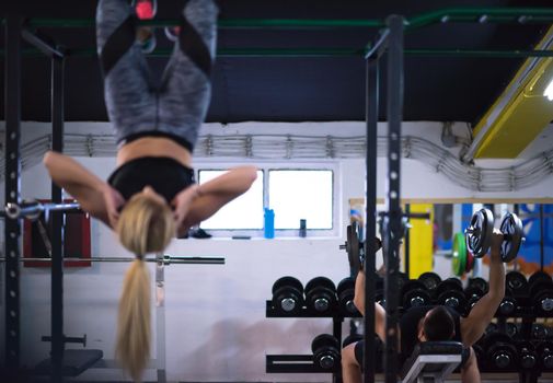athlete woman doing abs exercises hanging upside down on horizontal bar at cross fitness gym