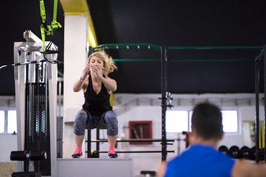 young athletic woman training with personal trainer  jumping on fit box at cross fitness gym