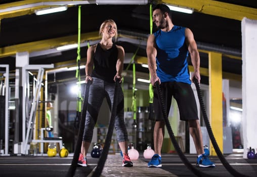 young fit sports couple working out in functional training gym doing  battle ropes cross fitness exercise