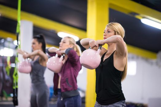 group of healthy young athletes doing exercises with kettlebells at cross fitness studio