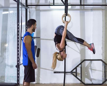 young athletic woman working out with personal trainer on gymnastic rings at the crossfitness gym