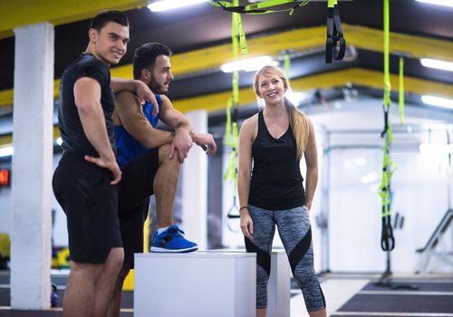 group of young healthy athletic people training jumping on fit box at cross fitness gym