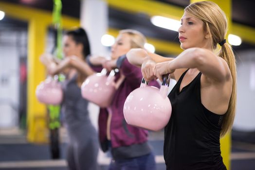 group of healthy young athletes doing exercises with kettlebells at cross fitness studio