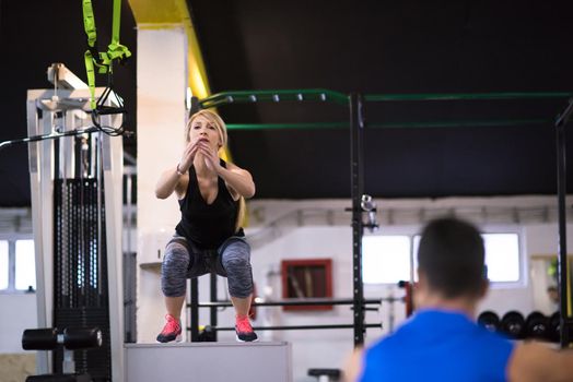 young athletic woman training with personal trainer  jumping on fit box at cross fitness gym