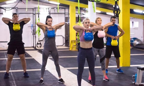 group of healthy young athletes doing exercises with kettlebells at cross fitness studio