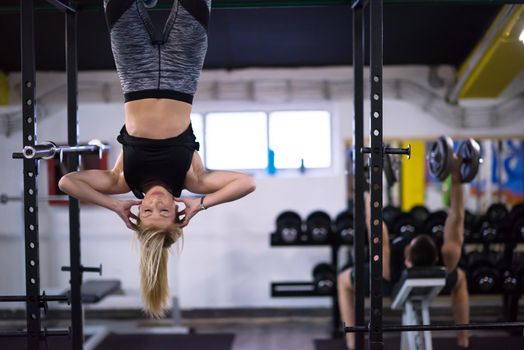 athlete woman doing abs exercises hanging upside down on horizontal bar at cross fitness gym