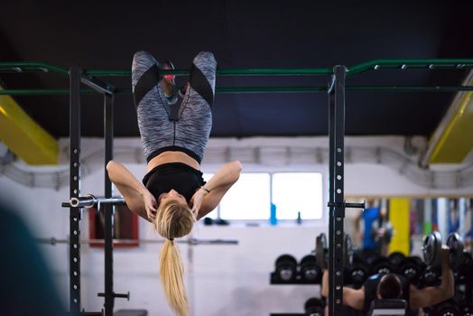 athlete woman doing abs exercises hanging upside down on horizontal bar at cross fitness gym