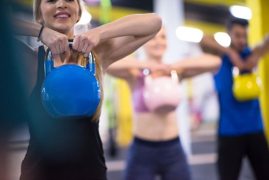 group of healthy young athletes doing exercises with kettlebells at cross fitness studio