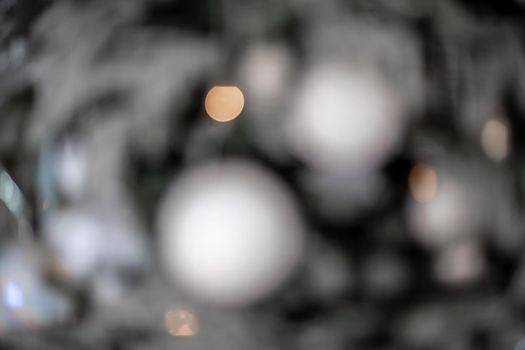 Close-up of a festively decorated outdoor Christmas tree with balls on a blurred sparkling fairy background. Defocused garland lights, bokeh effect