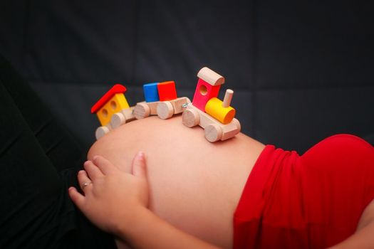 Kids wooden train toy on a pregnant belly. Baby expectation concept.