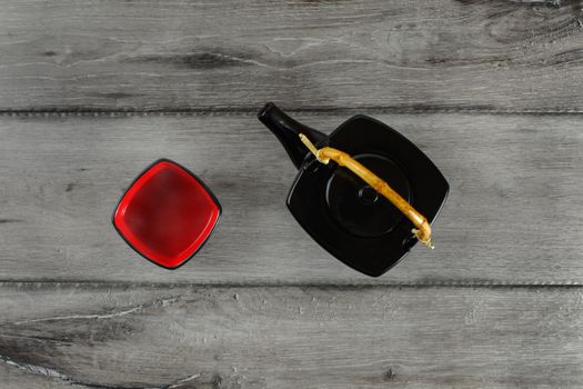 Table top view on black teapot and red square shaped cup of hot tea placed on gray wood desk.