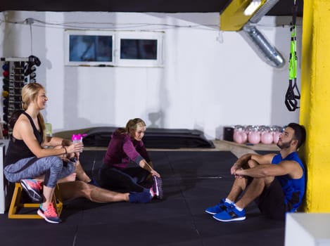 a group of young athletes sitting on the floor and relaxing after exercise at fitness gym
