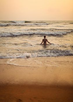 Silhouette of young woman going into the sea with small waves during golden evening light just after the sunset.