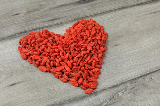 Heap of goji berry (wolfberry - Lycium chinense) dried fruits arranged in shape of heart on a gray wood table.