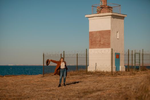 A woman walking along the coast near the sea. An elegant lady in a brown coat and a hat with fashionable makeup walks on the seashore.