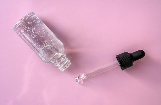 Opened transparent glass dropper bottle with air bubbles on pink background. Pipette with fluid hyaluronic acid, serum, retinol. Cosmetics and healthcare concept Flat lay. Luxury beauty product