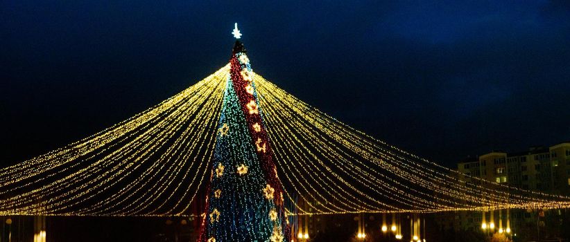 Long exposure night shot of a uniquely decorated main Christmas tree in the square after rain with reflection