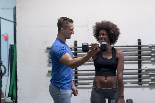 young beautiful African American woman doing bicep curls with fitness trainer in a gym