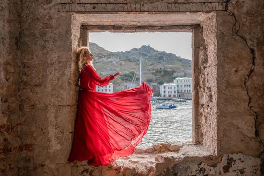 View of Balaklava Bay through an arched balcony in oriental style. The girl in a long red dress stands with her back. Abandoned mansion on the Black Sea coast.