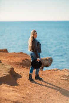 A blonde in a stylish black leather jacket walks along the seashore