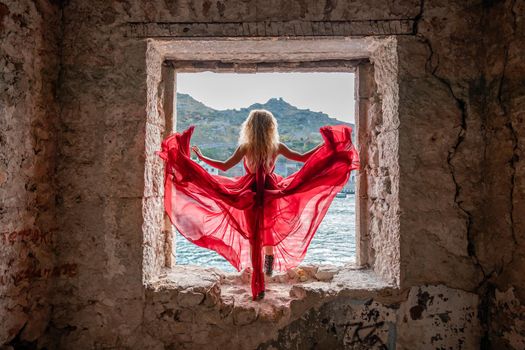 View of Balaklava Bay through an arched balcony in oriental style. The girl in a long red dress stands with her back. Abandoned mansion on the Black Sea coast.